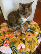 Load image into Gallery viewer, A small tortoiseshell cat sitting on a minky cat mat positioned on a chair. The cat mat is a cottage garden design and the cat is sitting up