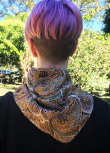 Load image into Gallery viewer, Beautiful soft and drapey rayon bandanna scarves in a timeless paisley designs, featuring a multitude of colours including mustard, teal and cobalt blue. A very spring fashion accessory for both humans and fur babies. Picture shows person with pink hair wearing as a neck scarf outside on a sunny day.
