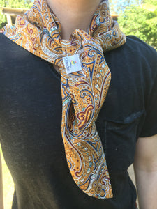 Beautiful soft and drapey rayon bandanna scarves in a timeless paisley designs, featuring a multitude of colours including mustard, teal and cobalt blue. A very spring fashion accessory for both humans and fur babies. Picture shows person with pink hair wearing as a neck scarf outside on a sunny day.