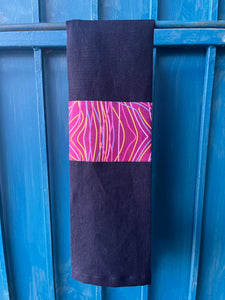 A navy blue tea towel made from European linen and featuring the art work Kokos String by Australian Indigenous artist Audrey Napanangka. The tea towel is hanging on a deep blue coloured wall.