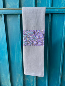 A blue tea towel made from European linen and featuring the art work Meteors by Australian Indigenous artist Heather Kennedy. The tea towel is hanging on a deep blue coloured wall.