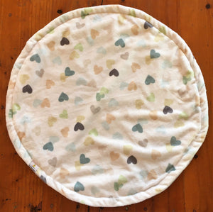 a round cat mat made with 3 layers of minky. Featuring small love hearts on a pale cream background. The love hearts are randomly placed and are muted colours of blue, pink brown and orange