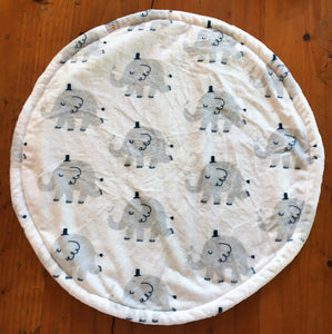a round cat mat made with 3 layers of minky. Featuring pale grey elephants parading in rows from right to left. The elephants are wearing tiny black top hats and have their tails in a semi upright position. The background is white.