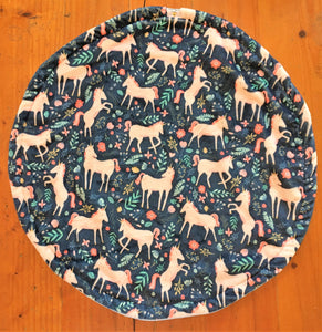 a round cat mat made with 3 layers of minky. Featuring prancing pink unicorns on a navy blue background and random tiny flowers and leaves in shades of blue, green and pink