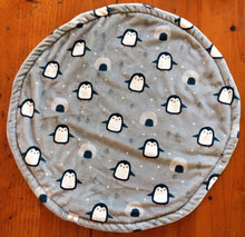 Load image into Gallery viewer, a round cat mat made with 3 layers of minky. Featuring a grey background with cute penguins walking with their wings out and little igloos and conifer trees in between