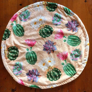 a round cat mat made with 3 layers of minky. Featuring an apricot coloured background and a variety of succulents, some of which are flowering. Flowers feature pink and daisy like colours