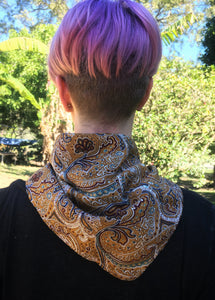 Beautiful soft and drapey rayon bandanna scarves in a timeless paisley designs, featuring a multitude of colours including mustard, teal and cobalt blue. A very spring fashion accessory for both humans and fur babies. Picture shows person with pink hair wearing as a neck scarf outside on a sunny day.