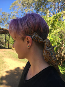 Beautiful soft and drapey rayon bandanna scarves in a timeless paisley designs, featuring a multitude of colours including mustard, teal and cobalt blue. A very spring fashion accessory for both humans and fur babies. Picture shows person with pink hair wearing  scarf to tie back the hair outside on a sunny day.