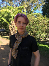 Load image into Gallery viewer, Beautiful soft and drapey rayon bandanna scarves in a timeless paisley designs, featuring a multitude of colours including mustard, teal and cobalt blue. A very spring fashion accessory for both humans and fur babies. Picture shows person with pink hair wearing as a neck scarf outside on a sunny day.