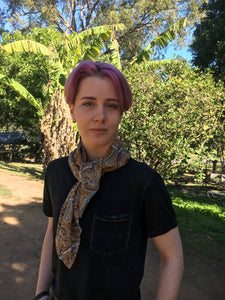 Beautiful soft and drapey rayon bandanna scarves in a timeless paisley designs, featuring a multitude of colours including mustard, teal and cobalt blue. A very spring fashion accessory for both humans and fur babies. Picture shows person with pink hair wearing as a neck scarf outside on a sunny day.